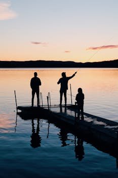 pexels-photo-988622-988622 A serene scene of a family fishing together on a lake dock at sunset, creating silhouettes on the water.