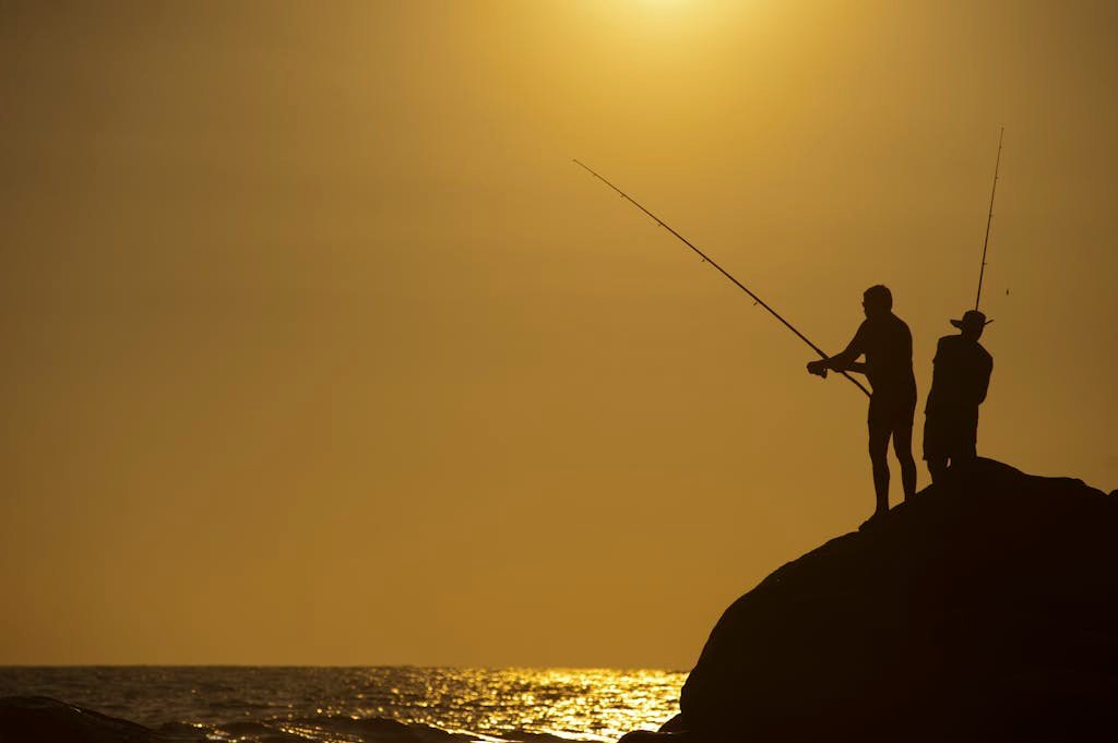 Beginner casting line casting lines at sunset by a rocky seashore, enjoying a peaceful evening.